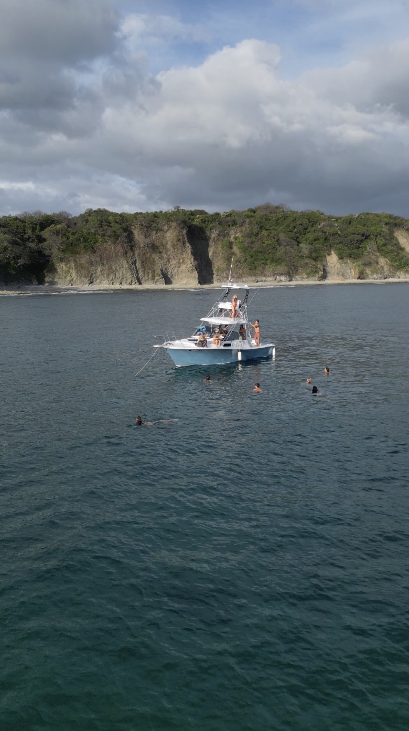 Monkey Head Adventures tour boat anchored below jungle cliffs, guests swimming around it